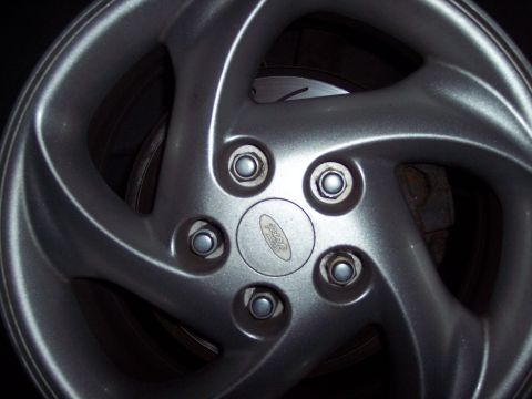 1995 Ford Probe - A close-up view of a silver five-spoke wheel with a Ford emblem and brake components.
