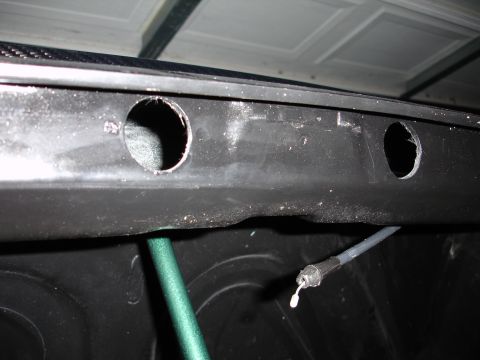 1993 Ford Taurus - A close-up view of a black plastic panel with two holes and a cable, possibly from a vehicle's trunk area.