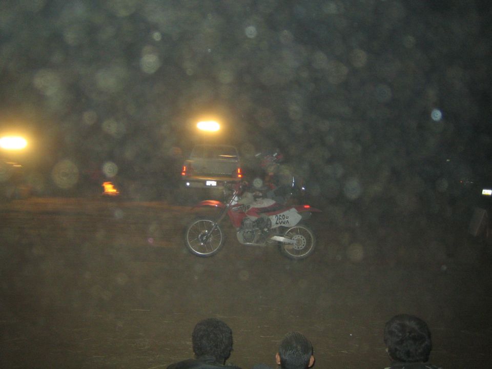 Red and white dirt bike racing across a dark dirt course at night with spectators watching