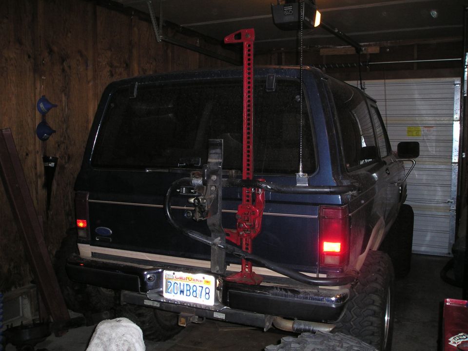Dark blue Ford SUV rear with swing-out carrier and red Hi-Lift jack in a garage