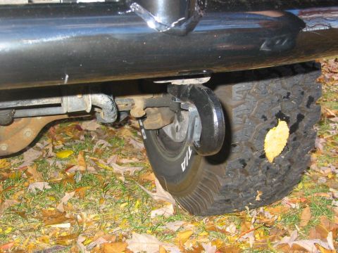 1996 Ford Bronco - Low-angle night shot under the rocker of a dark green truck, showing a black tube step or nerf bar, the leaf-spring shackle and shock mount…