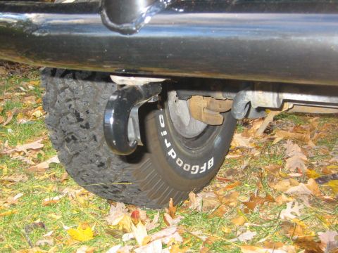 1996 Ford Bronco - Ground-level view under a black tube side step showing a BFGoodrich raised-white-letter tire, leaf-spring shackle, and the rear axle/suspen…