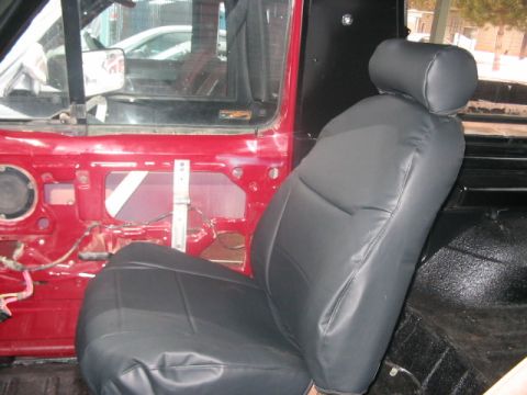 1991 Ford Bronco - The interior of a red vehicle shows black seat covers and a disassembled door panel, with another vehicle visible through the window.