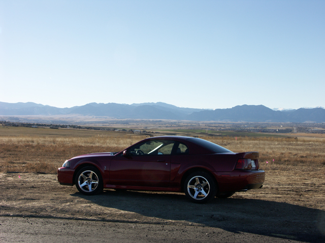 Red coupe with a spoiler parked on a dirt road with mountains in the background