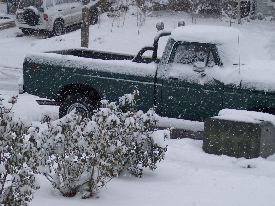 Dark green long-bed pickup covered in snow, side view with roof spotlights