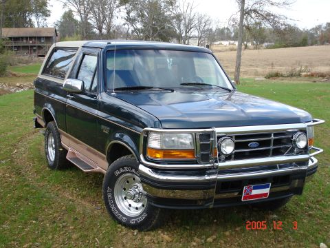 1995 Ford Bronco - This Ford Bronco is parked on a grassy area with trees and a building in the background.