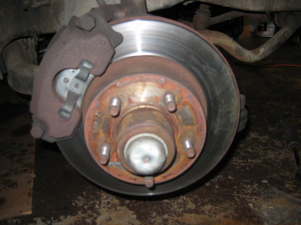Front brake rotor and caliper assembly with rust on the hub and caliper. Sway bar visible in background