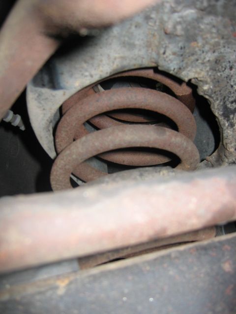 1985 Ford LTD Crown Victoria - Close-up of rusted suspension components, including a coil spring, with no visible vehicle identification.