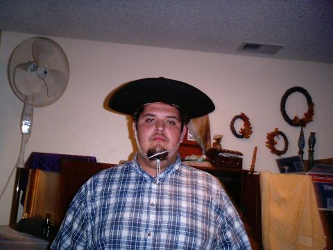 1986 Ford Bronco - Indoor portrait of a person in a blue plaid shirt wearing a black wide-brim hat, standing in a living room with a pedestal fan, wall wreath…