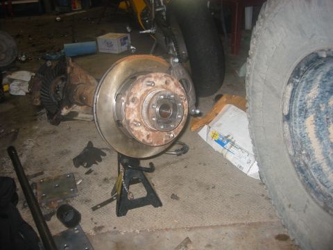1989 Ford Bronco - A disassembled differential and brake assembly is shown, supported by jack stands in a garage setting.