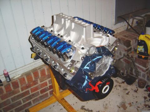 1986 Ford Bronco - A V8 engine with blue valve covers and a silver intake manifold is displayed on a yellow engine stand.