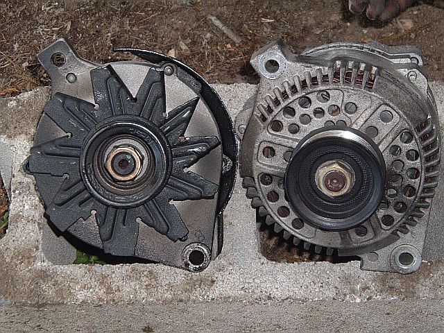 Two alternators side by side on a cinder block, older finned unit and newer compact unit