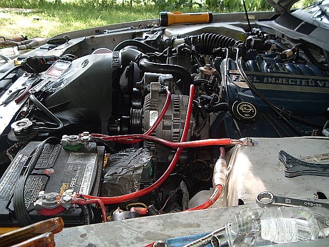 Fuel-injected V6 Ford engine bay with alternator and red high-amp cabling, tools nearby