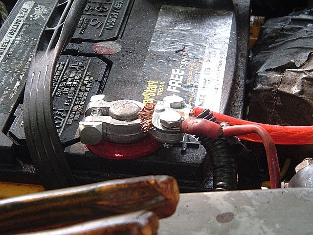 Close-up of a battery terminal with wire-brushed post, clamp, and red cable attached