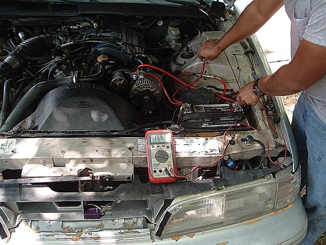 Man testing a Ford engine bay with a Craftsman multimeter clipped to the battery and alternator