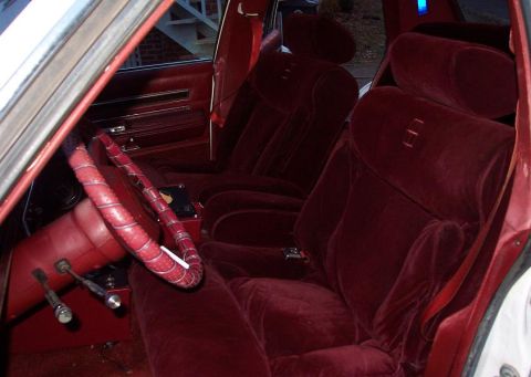 1985 Ford LTD Crown Victoria - The plush red velour interior of a car, bucket seats and a steering wheel.