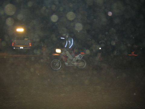 1990 Ford Bronco - helmeted rider on dirt bike 9 rides a dark course at night with a pickup truck parked behind under hazy lights.