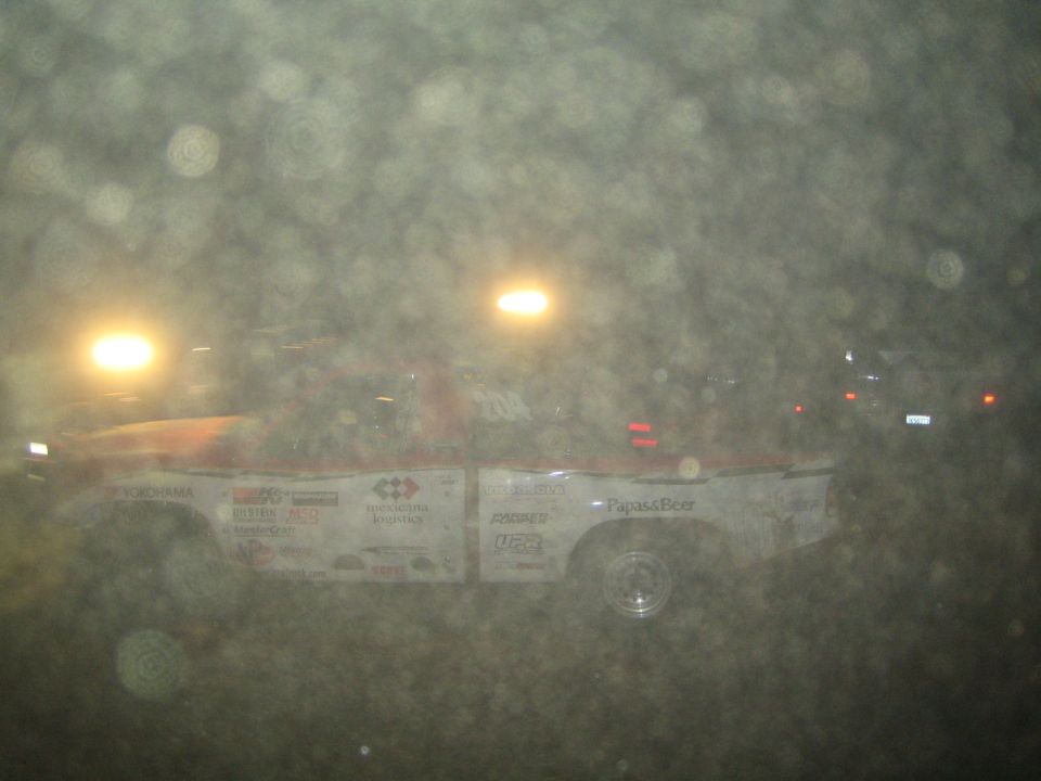 White off-road race truck with Yokohama and sponsor decals racing through dust at night