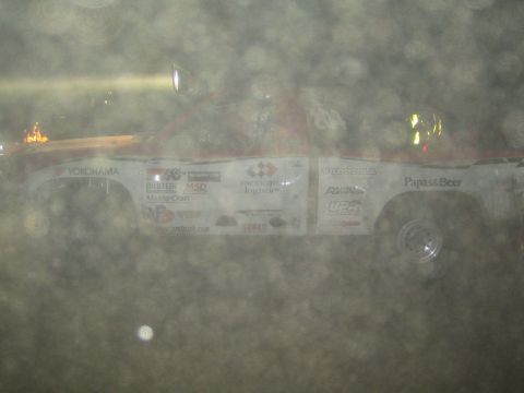 1990 Ford Bronco - white off-road race truck plastered with Yokohama and Papas and Beer decals sits in dusty night haze.
