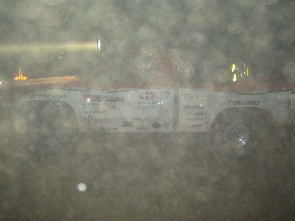 White off-road race truck with Yokohama, Papas and Beer decals seen through dusty haze at night
