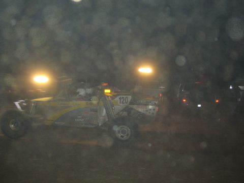 1990 Ford Bronco - yellow and white off-road race buggy numbered 120 races through dusty haze under night lights.