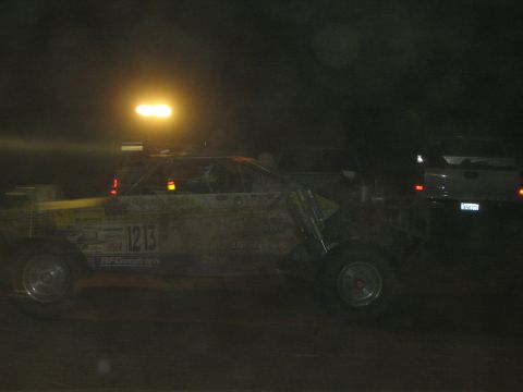 1990 Ford Bronco - yellow off-road race buggy marked 1213 with a BFGoodrich decal sits in profile at night beside a backlit truck.