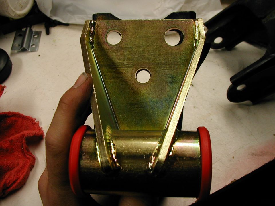 Hand holding gold zinc-plated welded mount bracket with red polyurethane bushings on a tube