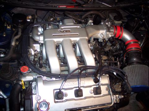 1995 Ford Probe - Close-up view of a V6 engine, showing the intake manifold, air filter, and 'Mazda' branding on the valve cover.