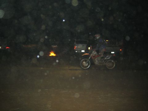 1990 Ford Bronco - motorcyclist on a number 426 dirt bike rides through a dark dusty desert course past a parked pickup truck at night.