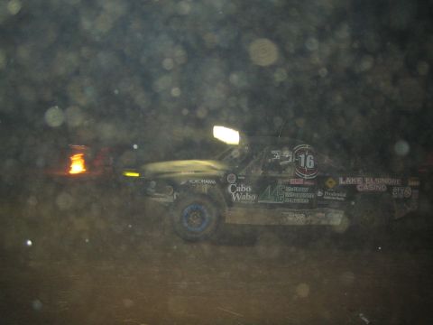 1990 Ford Bronco - dark off-road race truck marked 16 with Cabo Wabo and Lake Elsinore Casino decals sits in profile on a dusty night course.