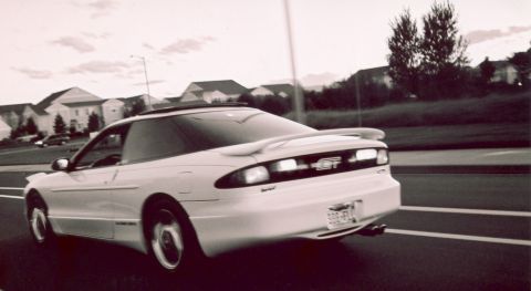 1996 Ford Probe - A white 1996 Ford Probe GT coupe drives down a suburban road, its rear spoiler visible.