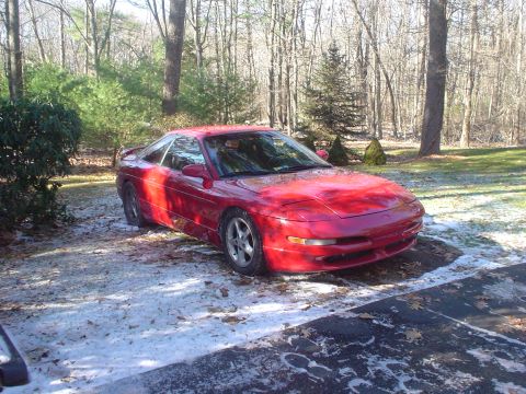1995 Ford Probe - A red 1995 Ford Probe sits in a driveway with patches of snow and fallen leaves.