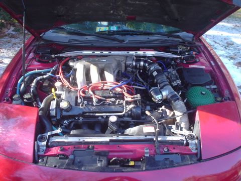 1995 Ford Probe - The engine bay of a red Ford Probe is visible with the hood open, revealing the engine and turbo components.