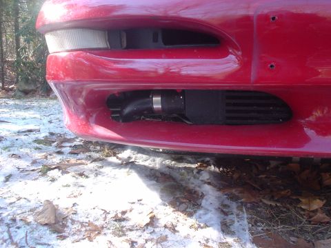 1995 Ford Probe - Close-up of a red car's front bumper reveals an aftermarket intercooler installed beneath the main grille opening.