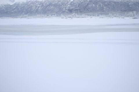 2003 Jeep TJ - A vast expanse of snow covers the land, with a frozen body of water in the mid-ground and snow-dusted mountains in the background.