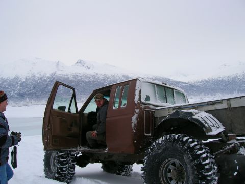 2003 Jeep TJ - Modified pickup truck with oversized tires sits in a snowy landscape with mountains behind.