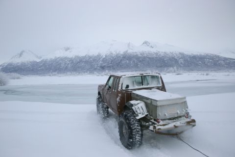 2003 Jeep TJ - A brown pickup truck navigates a snowy landscape with snow-covered mountains in the background.