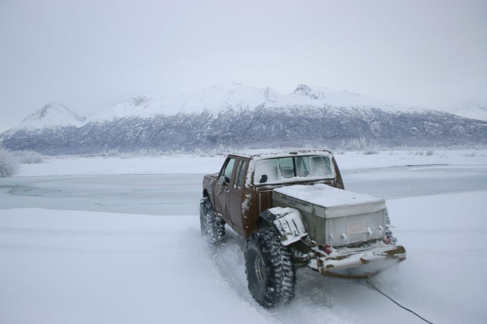 Brown pickup truck with large off-road tires and a toolbox in the bed, driving in snow