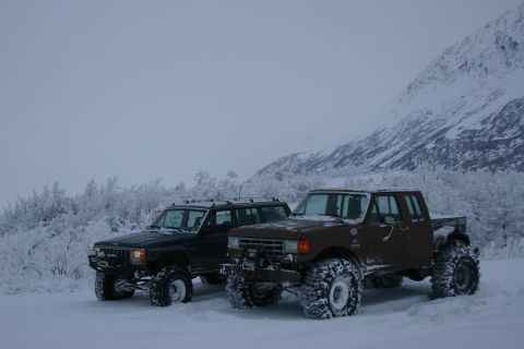 2003 Jeep TJ - Two modified off-road vehicles, a brown pickup and a black Jeep SUV, are parked in a snowy, mountainous area.
