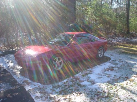1995 Ford Probe - A red 1995 Ford Probe coupe sits in a snowy outdoor setting, with sunlight creating lens flares across the image.