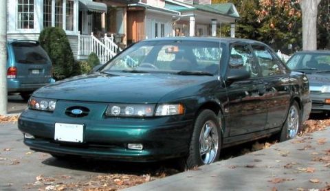 1993 Ford Taurus - A green sedan is parked on a street lined with houses and fallen leaves.