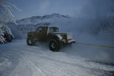 2003 Jeep TJ - A brown pickup truck is being towed in a snowy environment with mountains in the background.