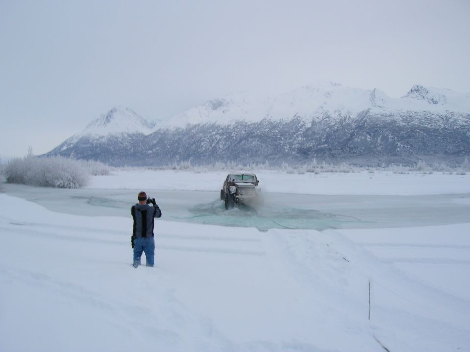 2003 Jeep TJ driving through shallow icy water with snow-covered mountains in background