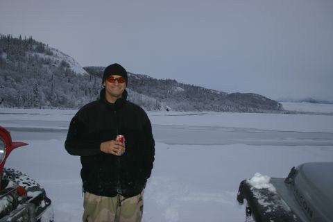 2003 Jeep TJ - A man holding a soda can stands in the snow next to a 2003 Jeep TJ Rubicon, with a frozen lake and snow-covered hills in the background.