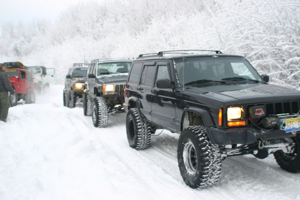 Black Jeep Cherokee in snow, front 3/4 view. License plate visible