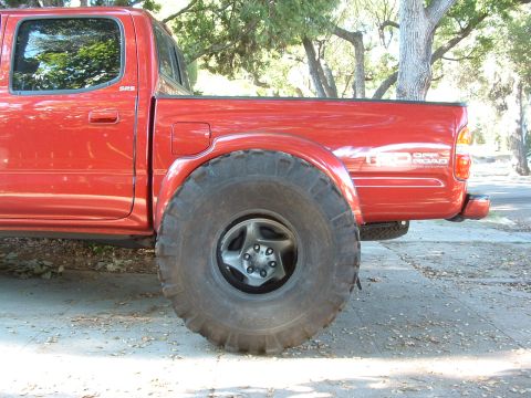 2004 Toyota Tacoma - This red Toyota Tacoma features oversized off-road tires, a common modification for this model.