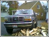 1993 Ford Bronco - A dark blue Ford Bronco is parked in a driveway, with firewood stacked in front of it.