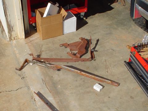 1984 Ford Bronco - Assorted rusted metal car parts are on the ground near a toolbox and storage boxes.