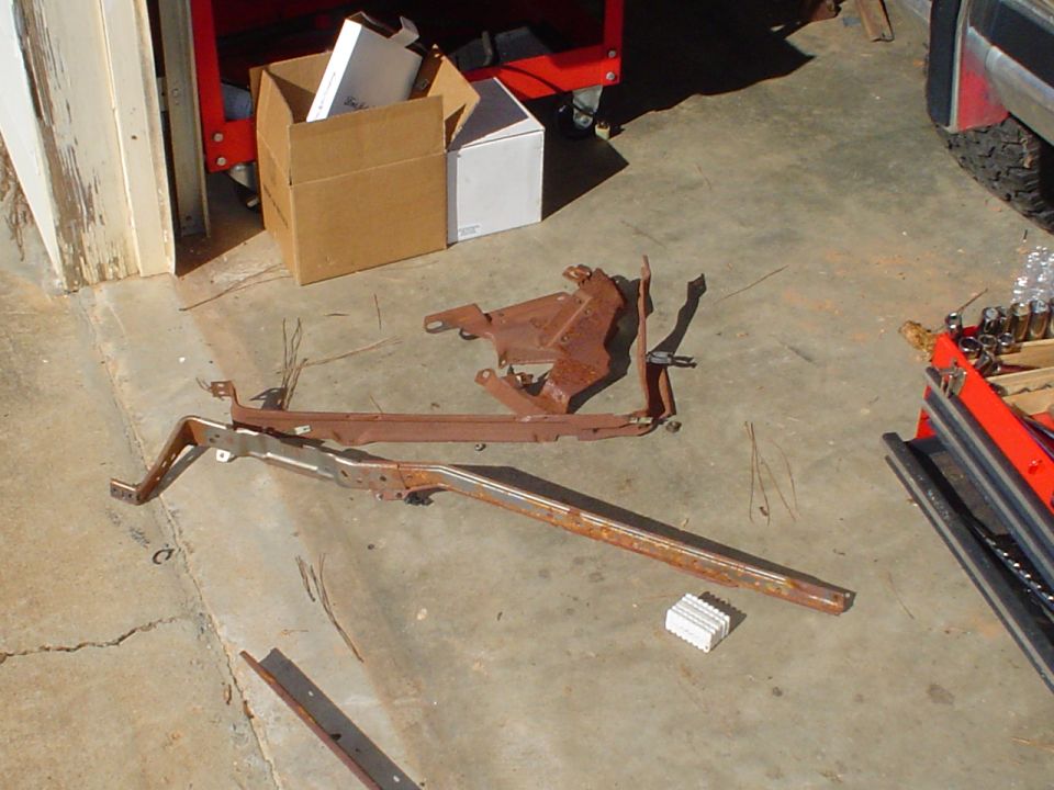 Rusted metal car parts, possibly from a dashboard or frame, laid out on a concrete floor next to a toolbox and boxes