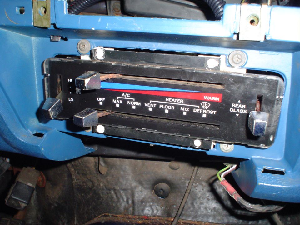 Close-up of a car's climate control panel with knobs for fan speed, A/C, heater, and defrost settings